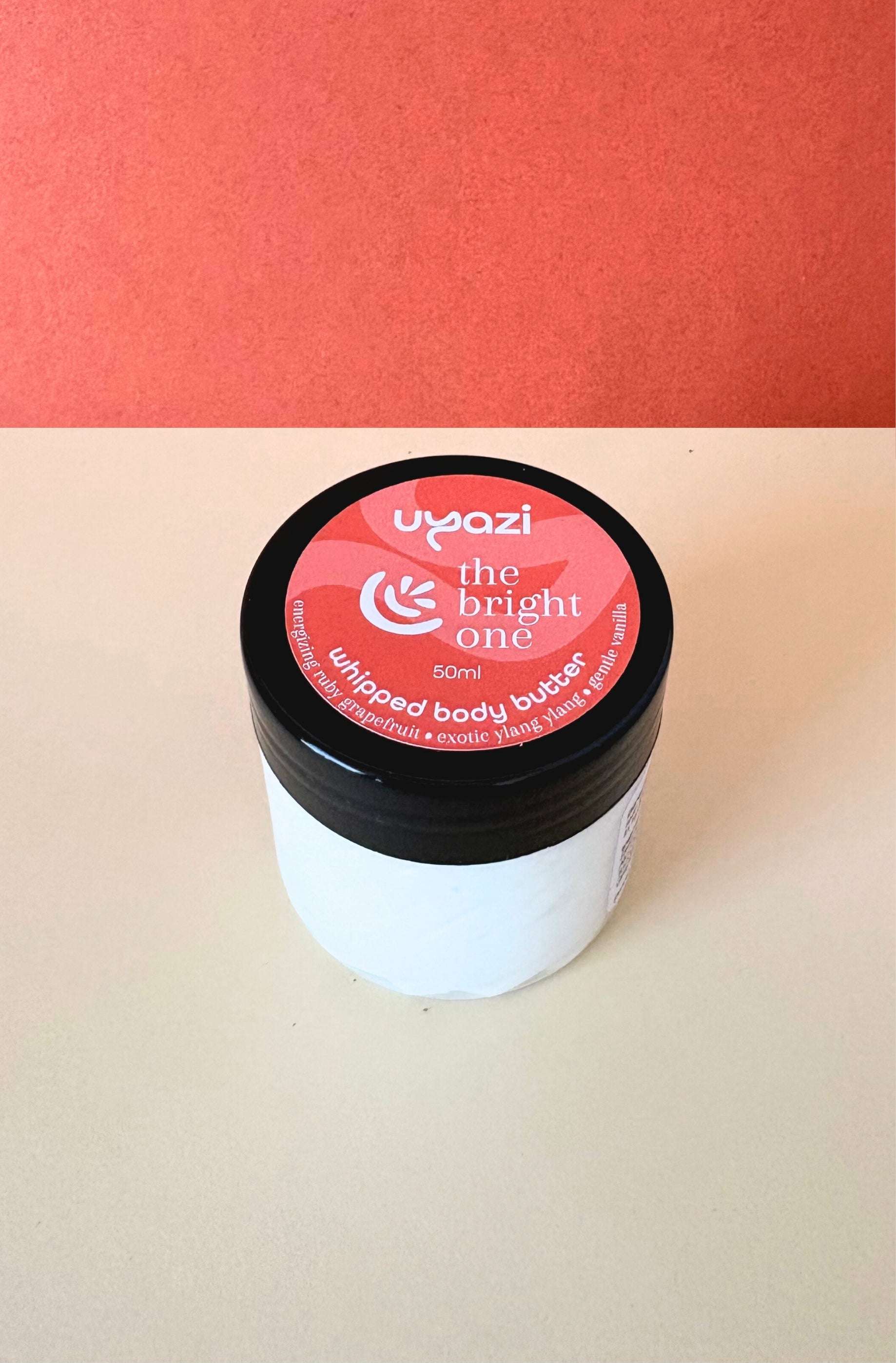Jar of 'the bright one' whipped body butter with a pink label on a beige surface.