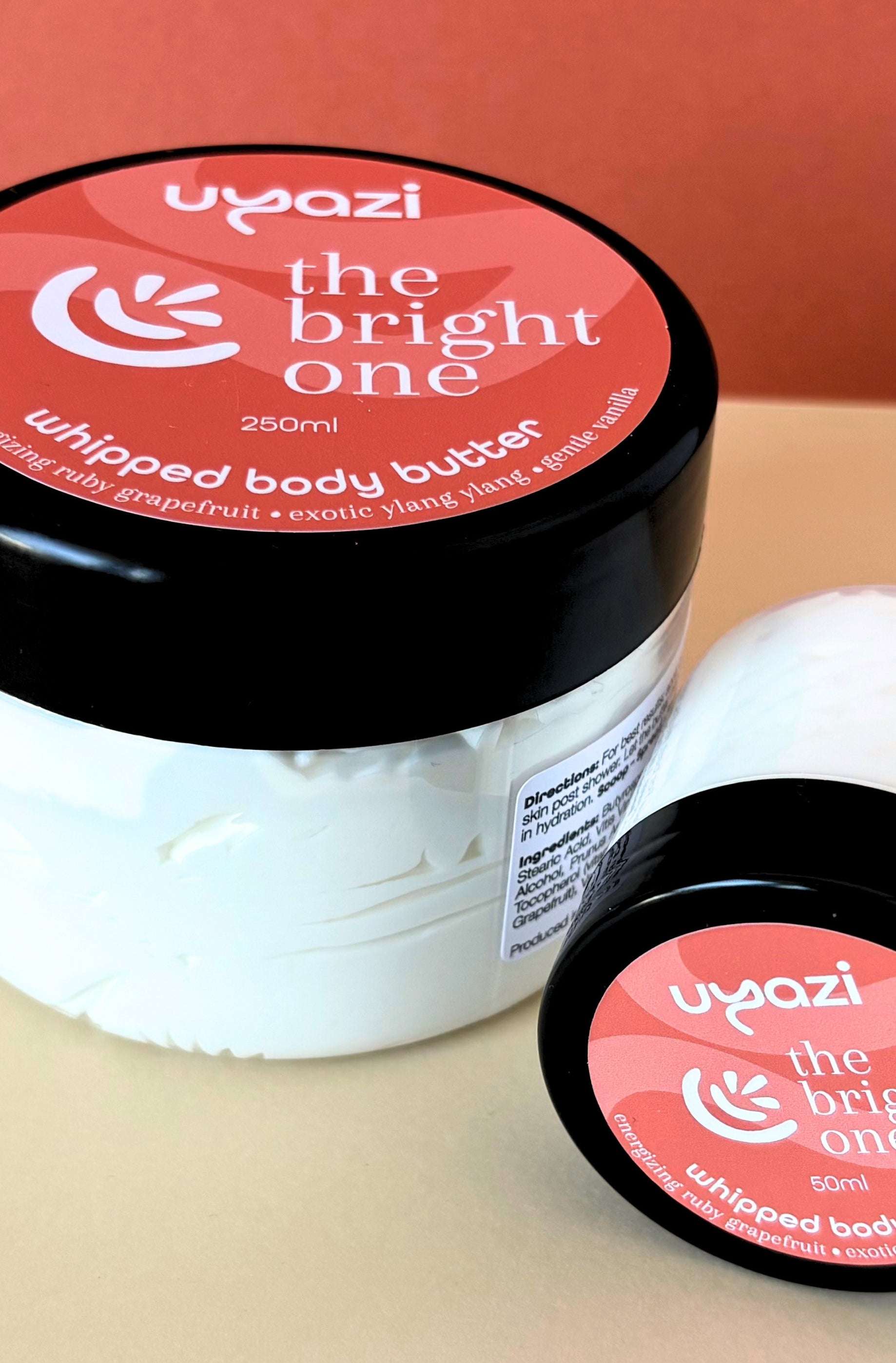 Uyazi whipped body butter jar with orange and peach label on a beige background