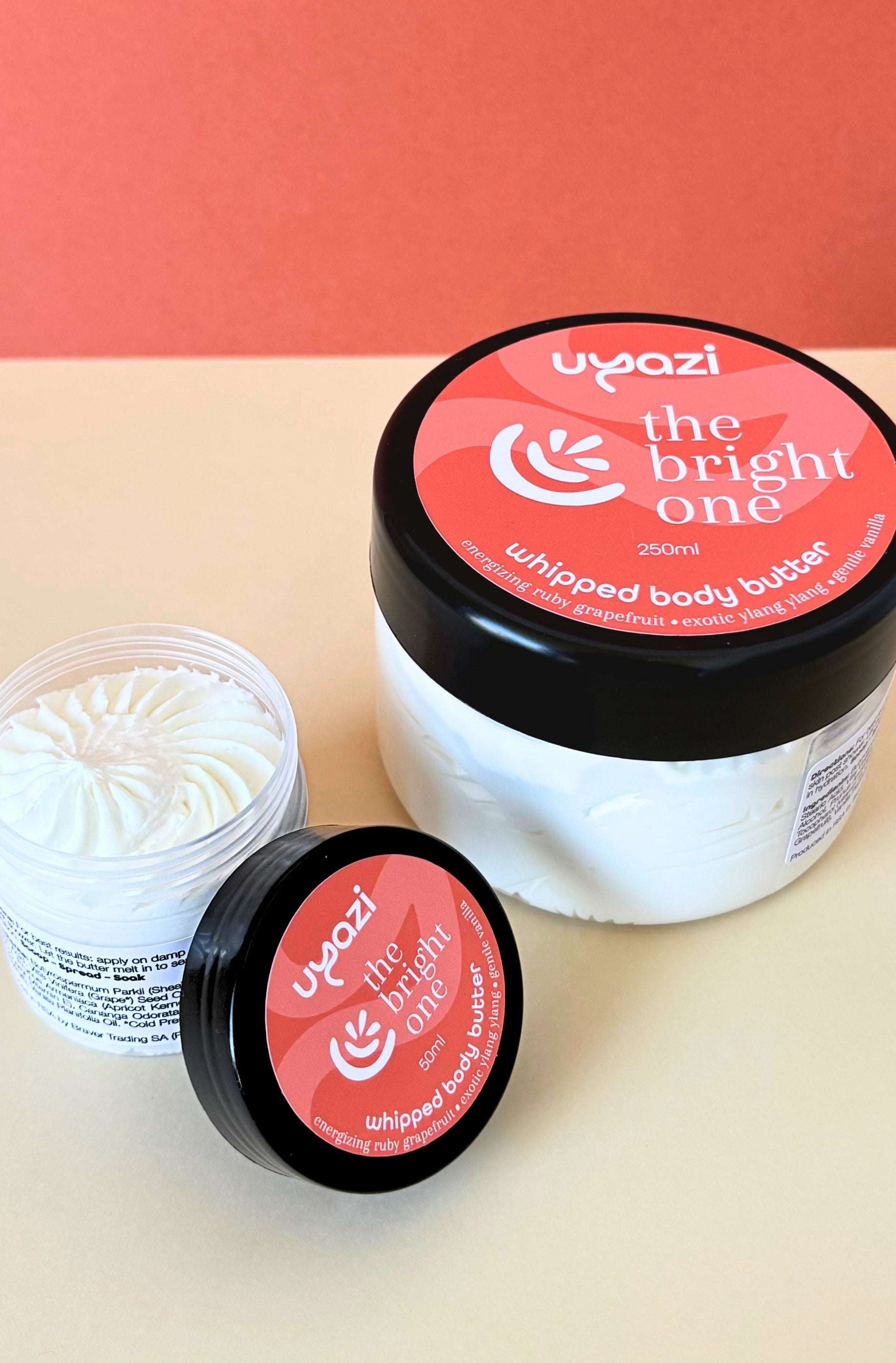 Two jars of 'the bright one' whipped body butter with an orange lid on a beige surface.