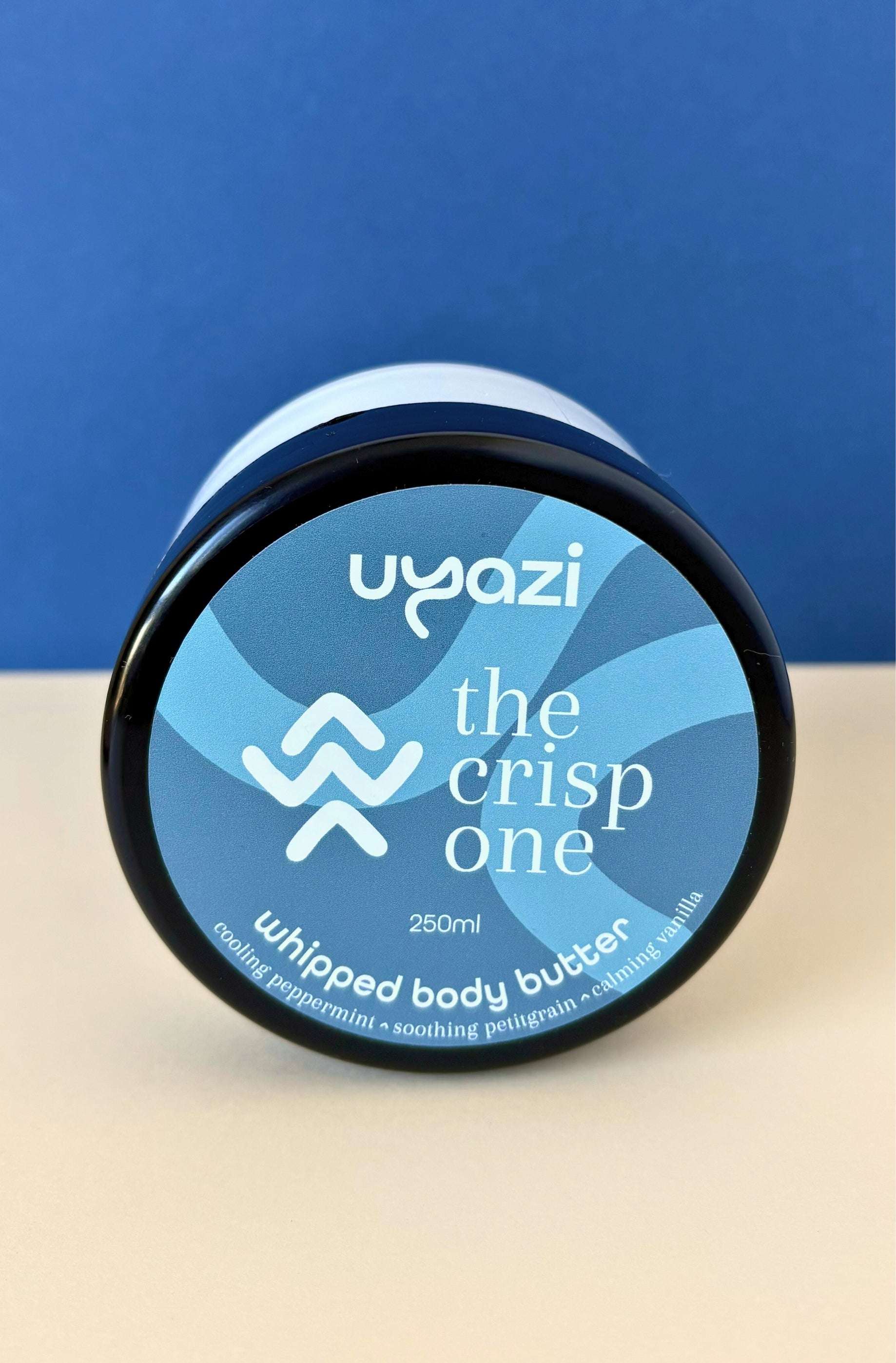 Uyazi whipped body butter 250ml container with blue label on a beige surface and blue background