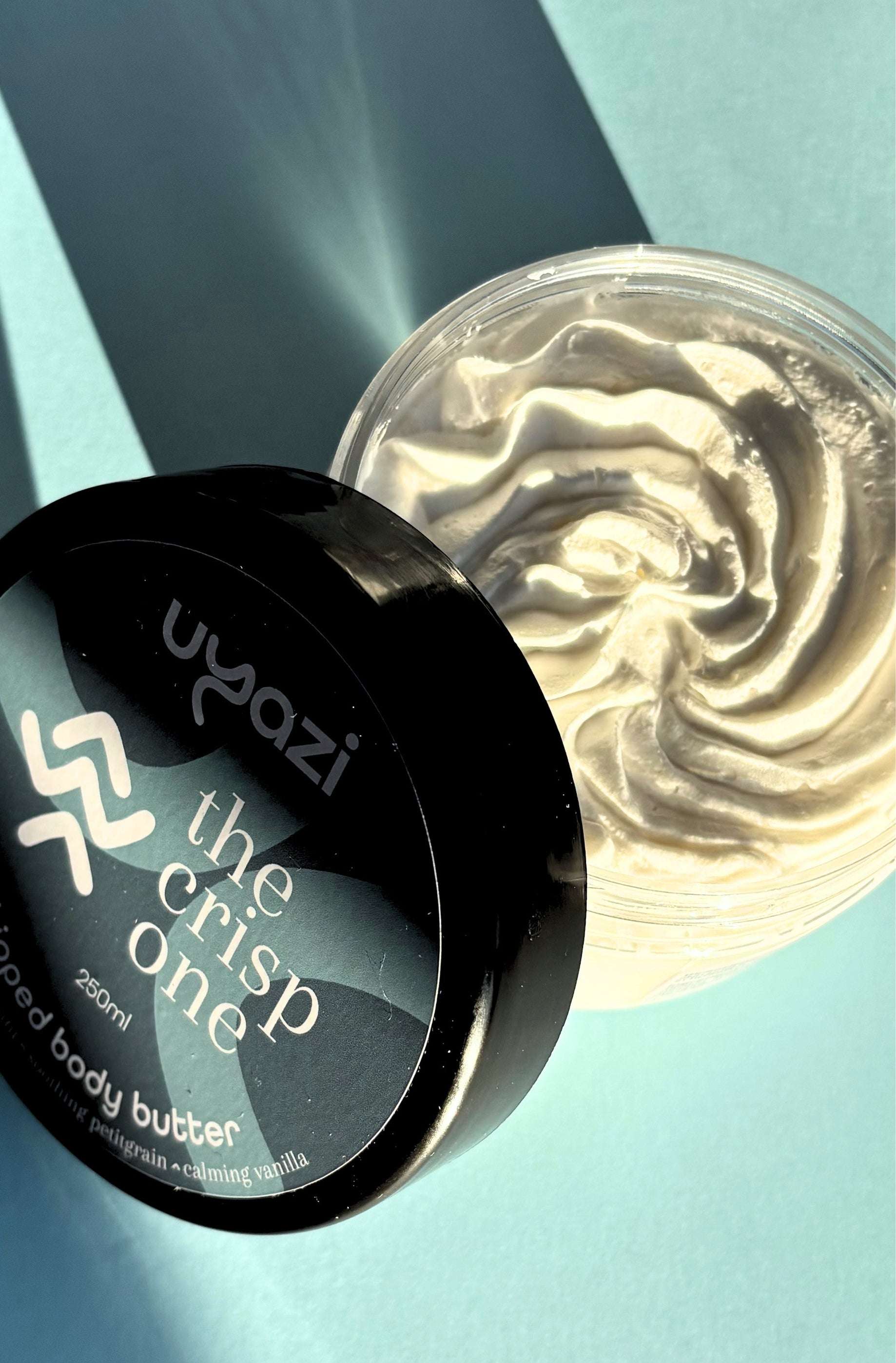 Body butter container labeled 'the crisp one' with visible brand name on a light blue background with shadow play