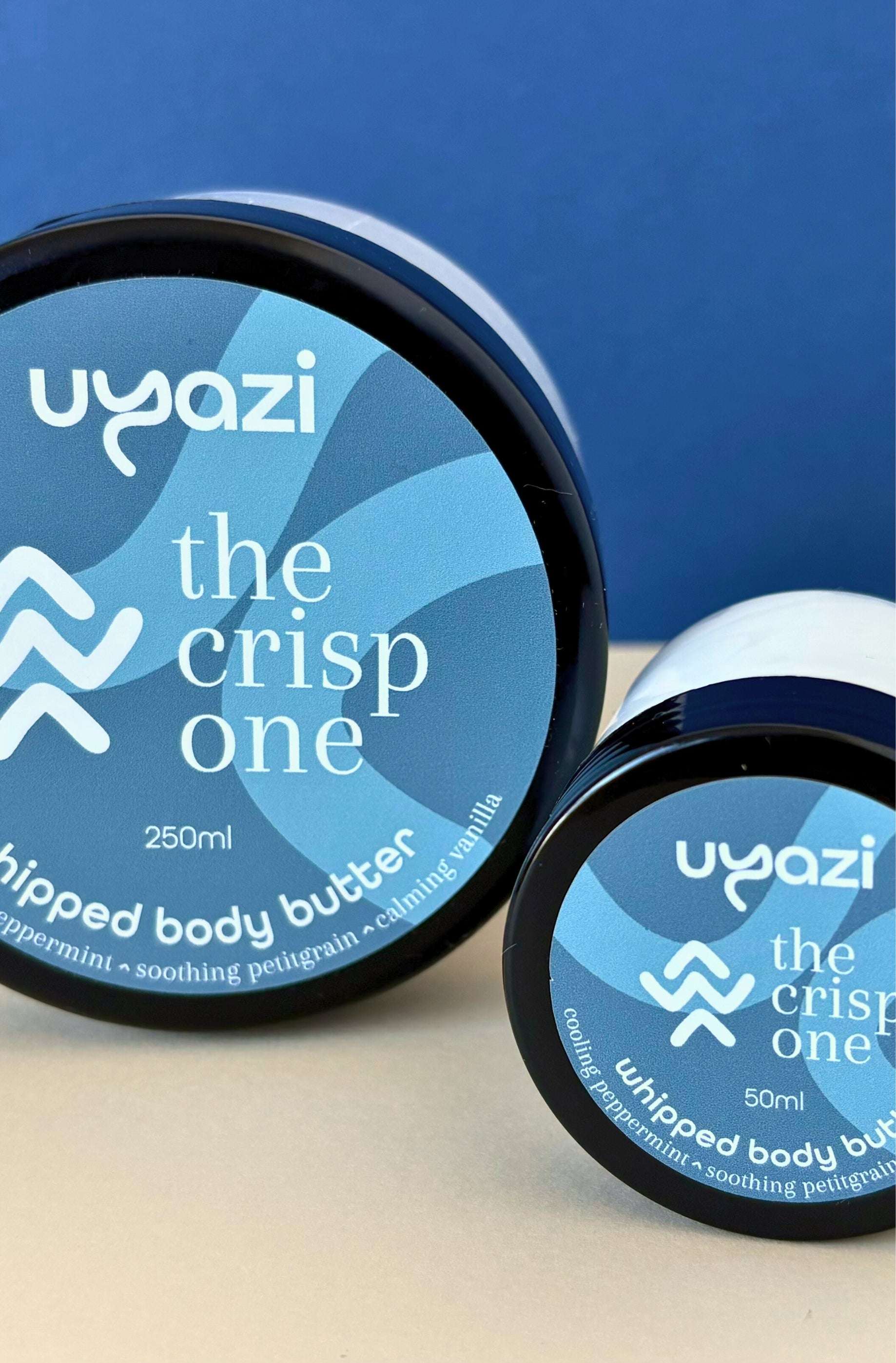 Two containers of Uyazi whipped body butter with blue labels on a blue background