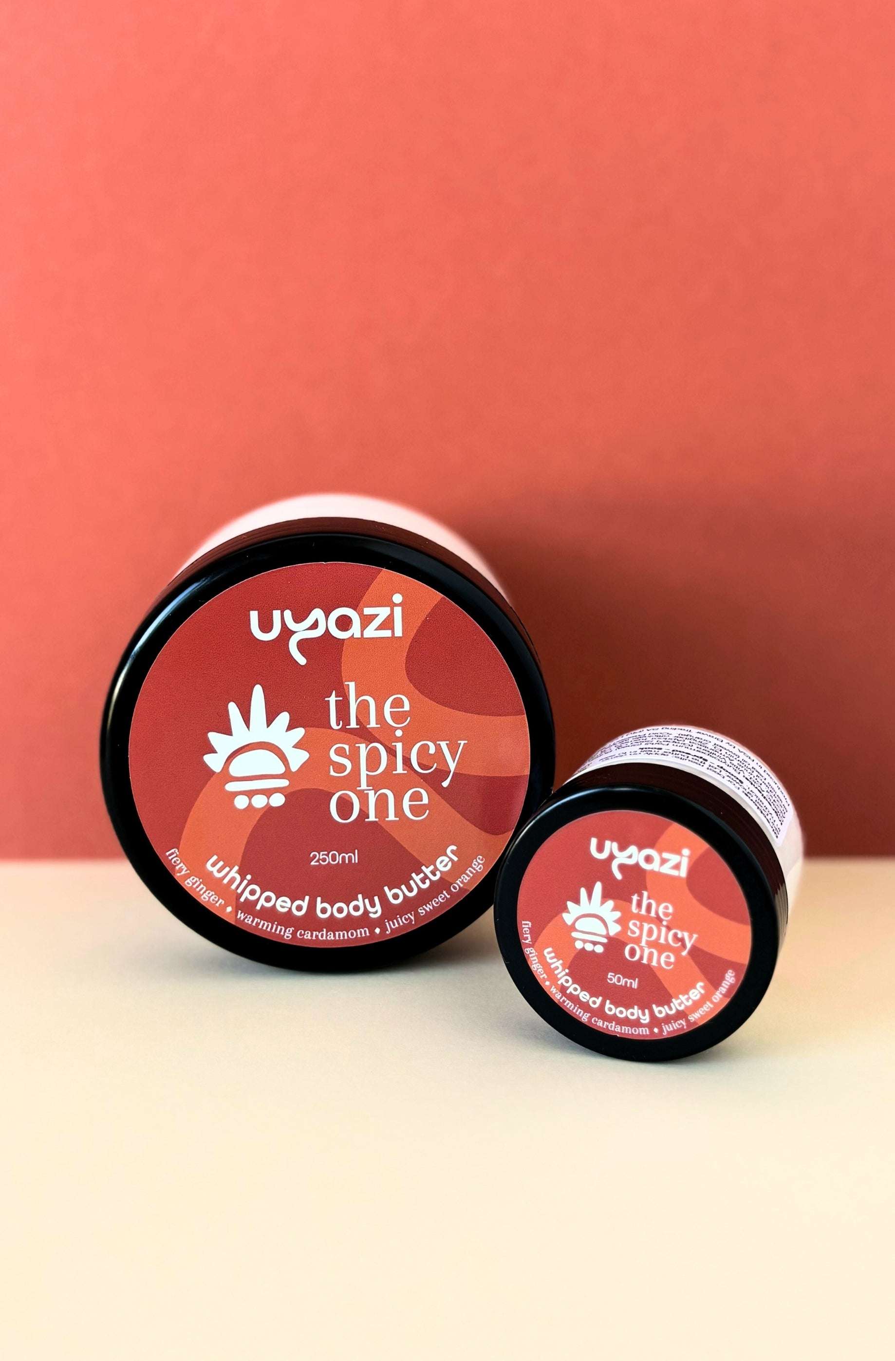 Two jars of Uyazi whipped body butter labeled 'the spicy one' on an orange background