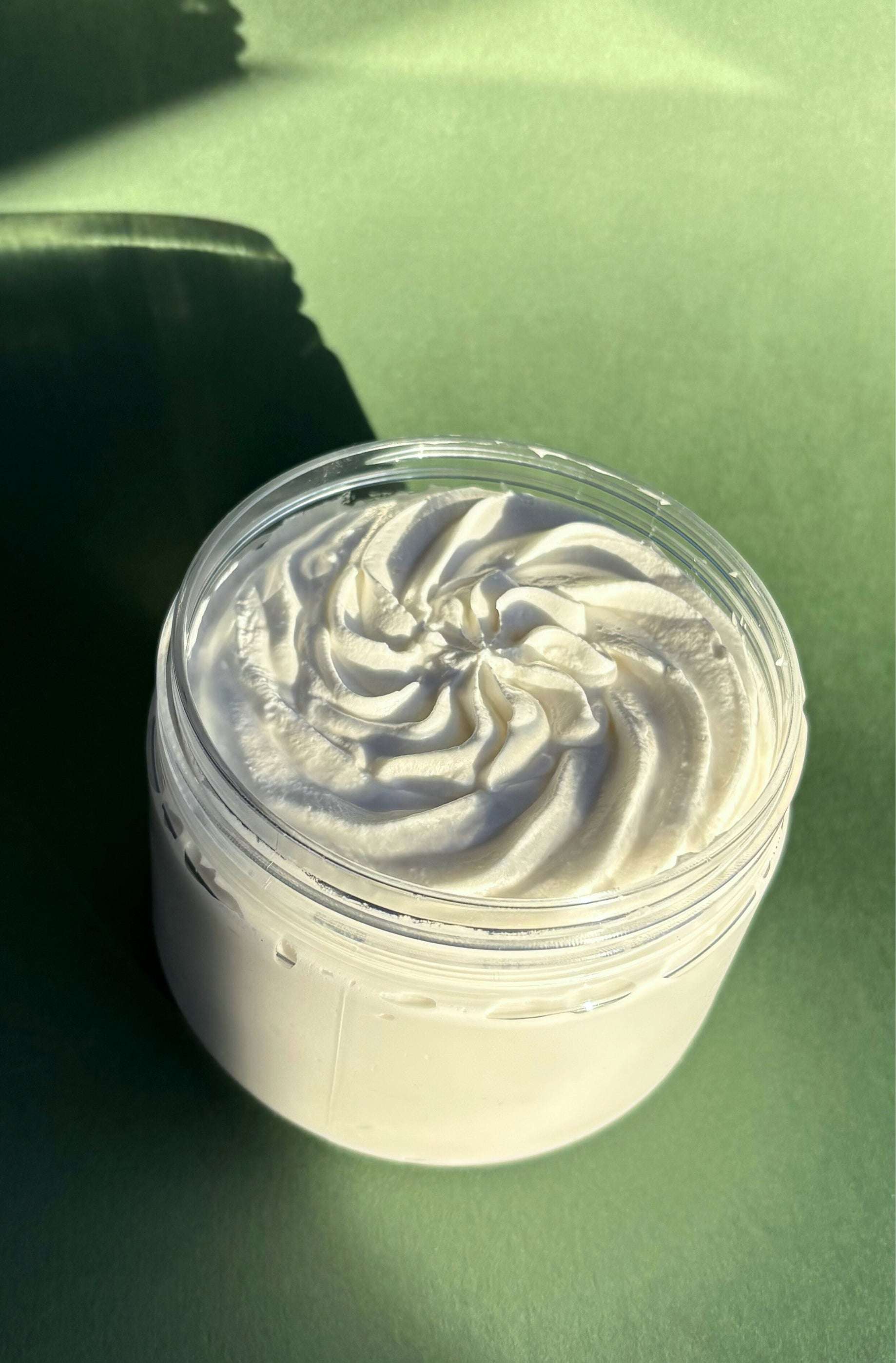 Jar of creamy whipped body butter with a decorative swirl pattern on a green surface