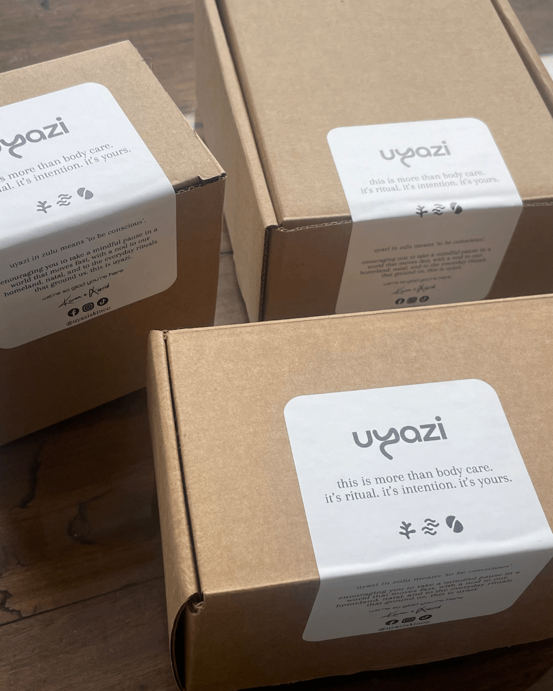 Three cardboard boxes packed with whipped body butters with 'uyazi' labels on a wooden surface