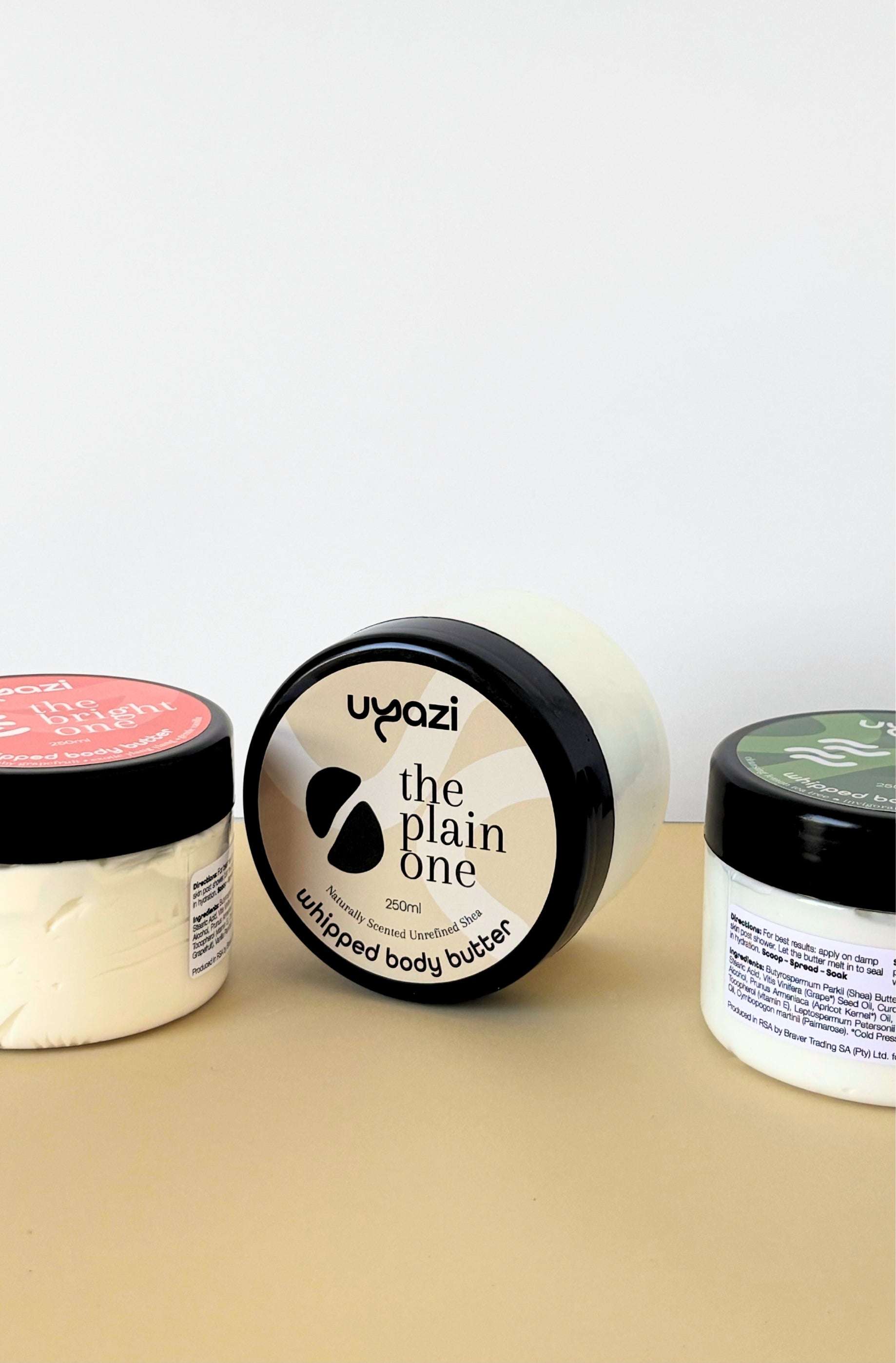Three containers of Uyazi body butter on a beige surface with a white background