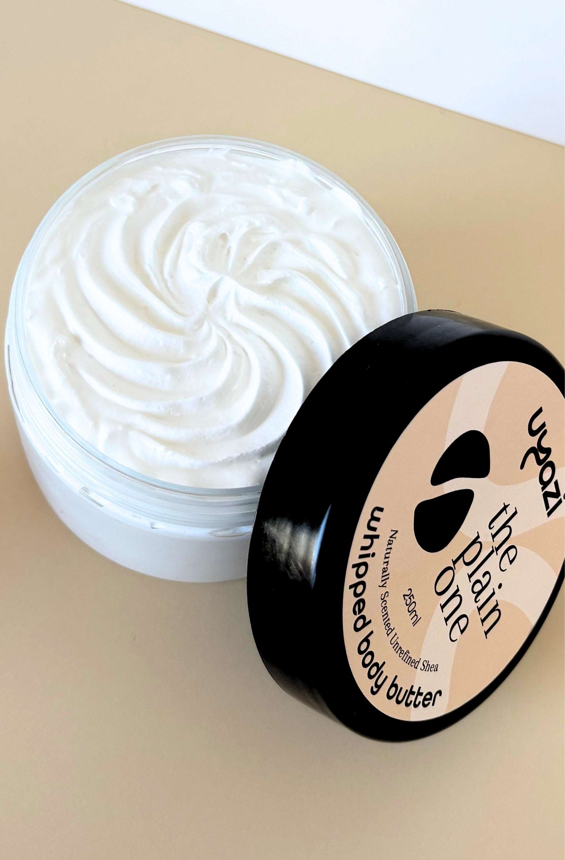 Whipped body butter jar with black lid on a beige background