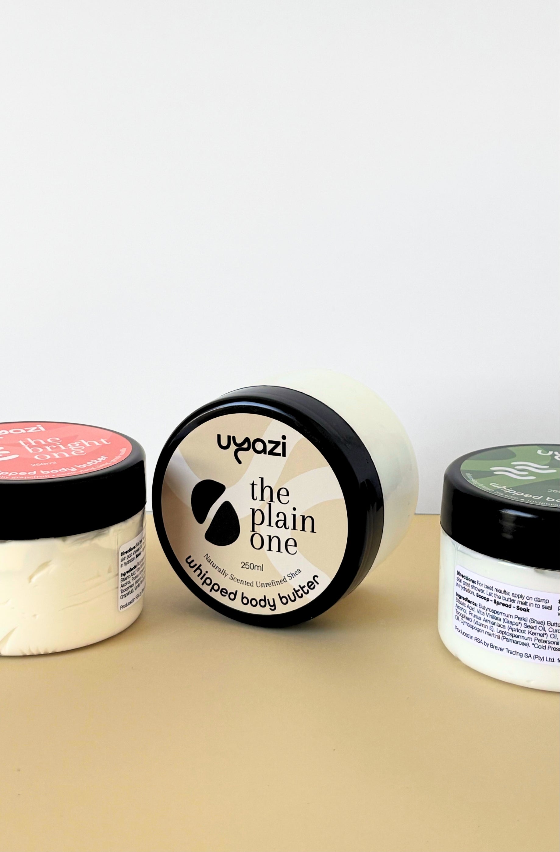 Three containers of Uyazi body butter on a beige surface with a white background