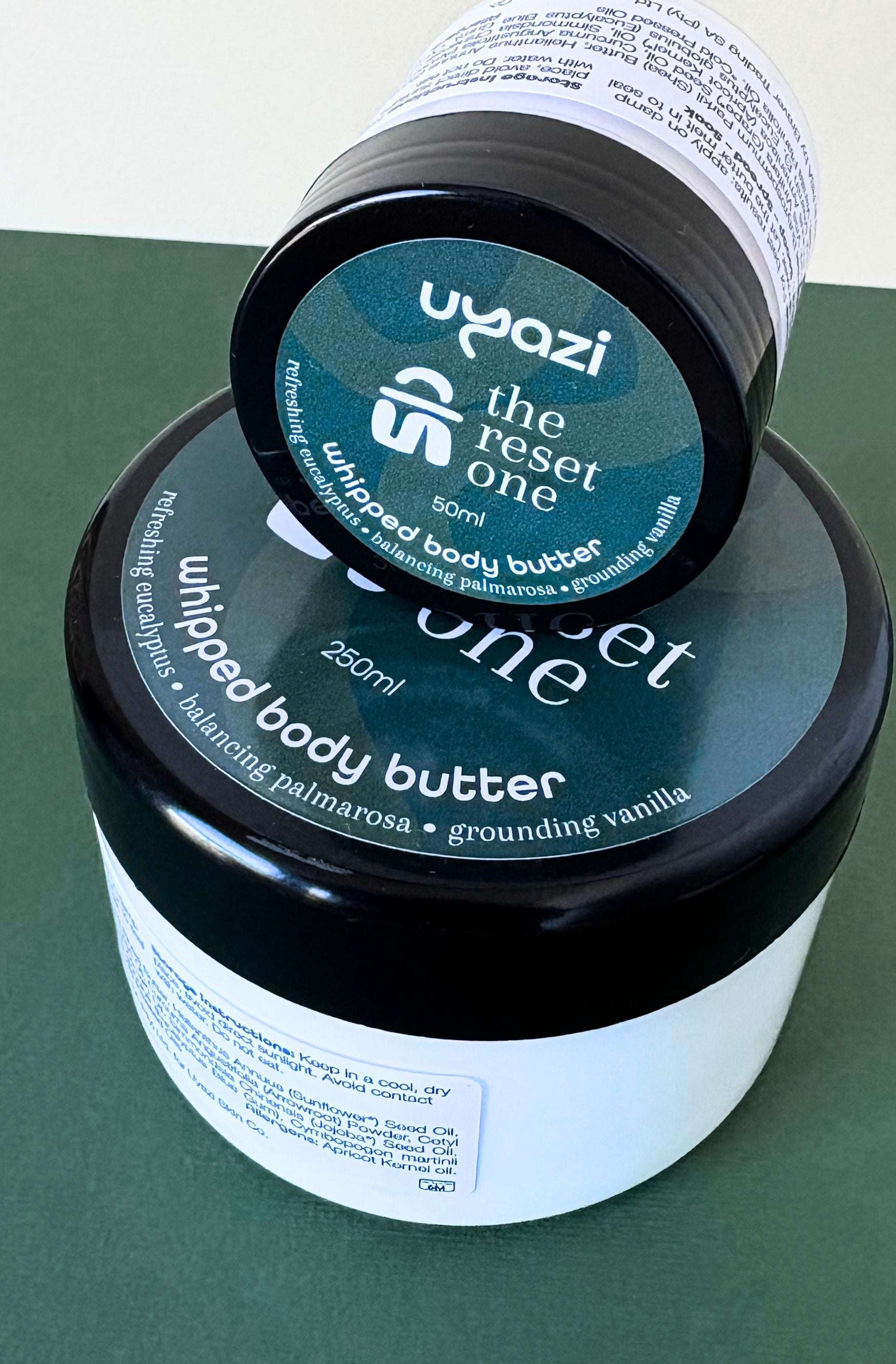 Two containers of Uyazi 'the reset one' whipped body butter on a green surface.