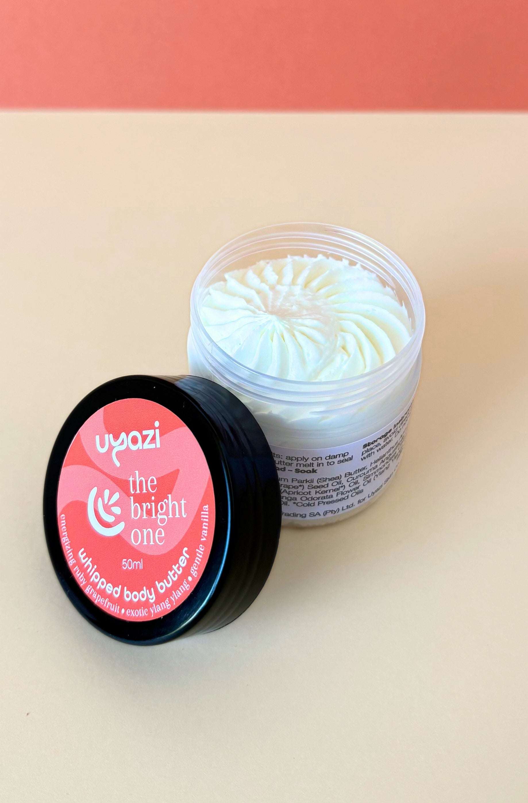 Jar of whipped body butter with orange label on a beige background