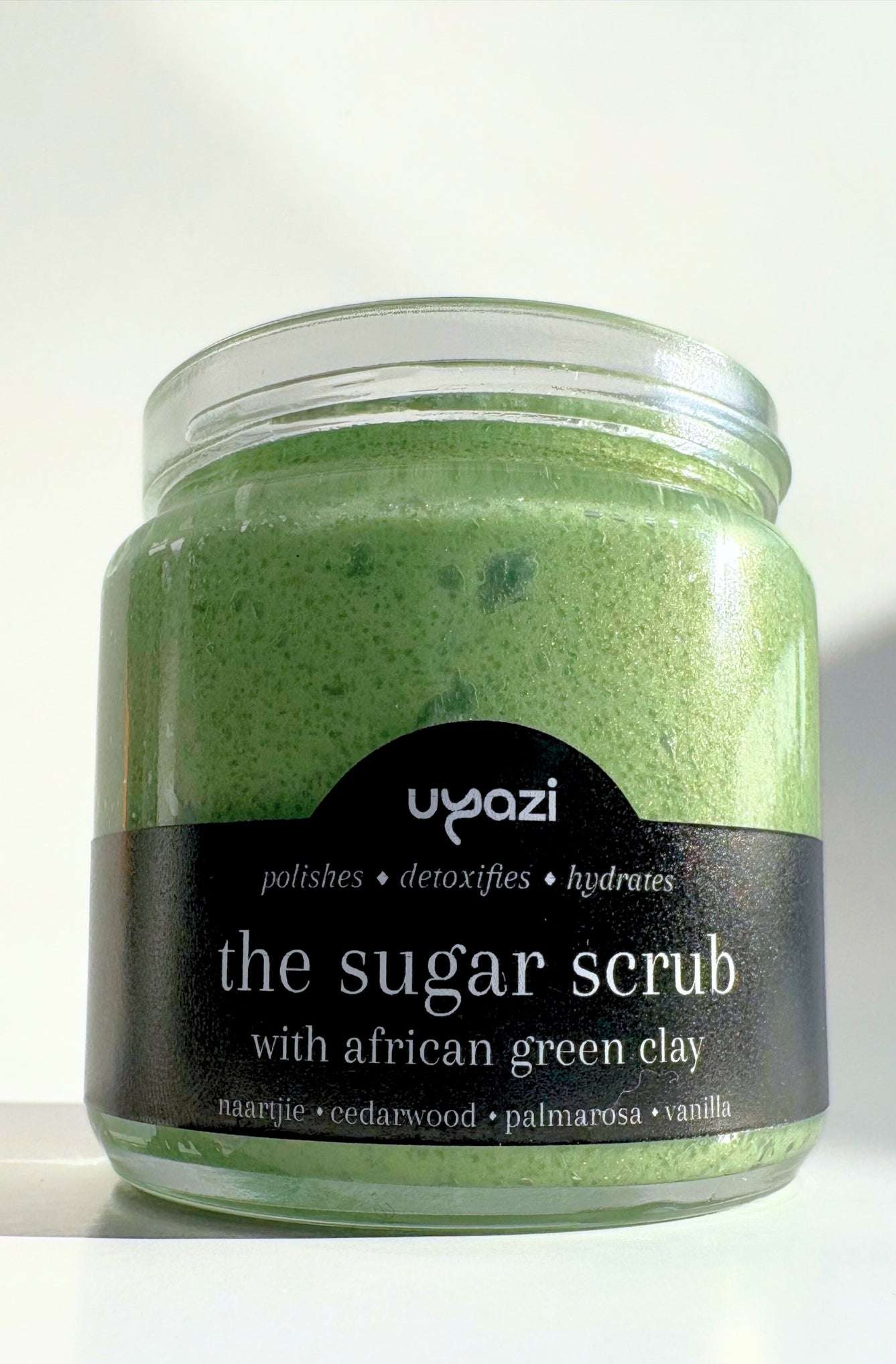 Jar of green sugar scrub with a black label on a white background