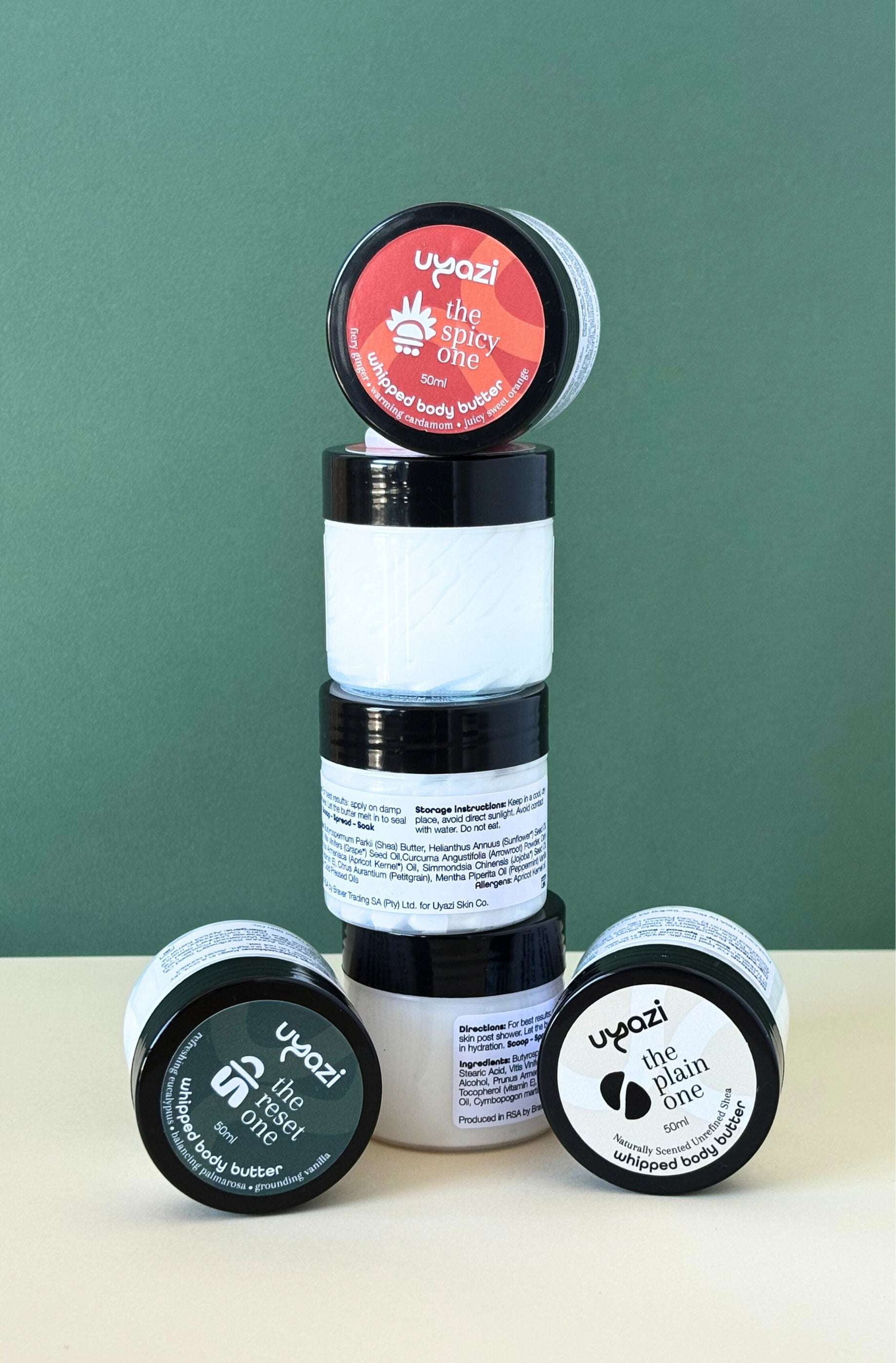 Stack of cosmetic jars filled with whipped body butter with visible branding on a green background