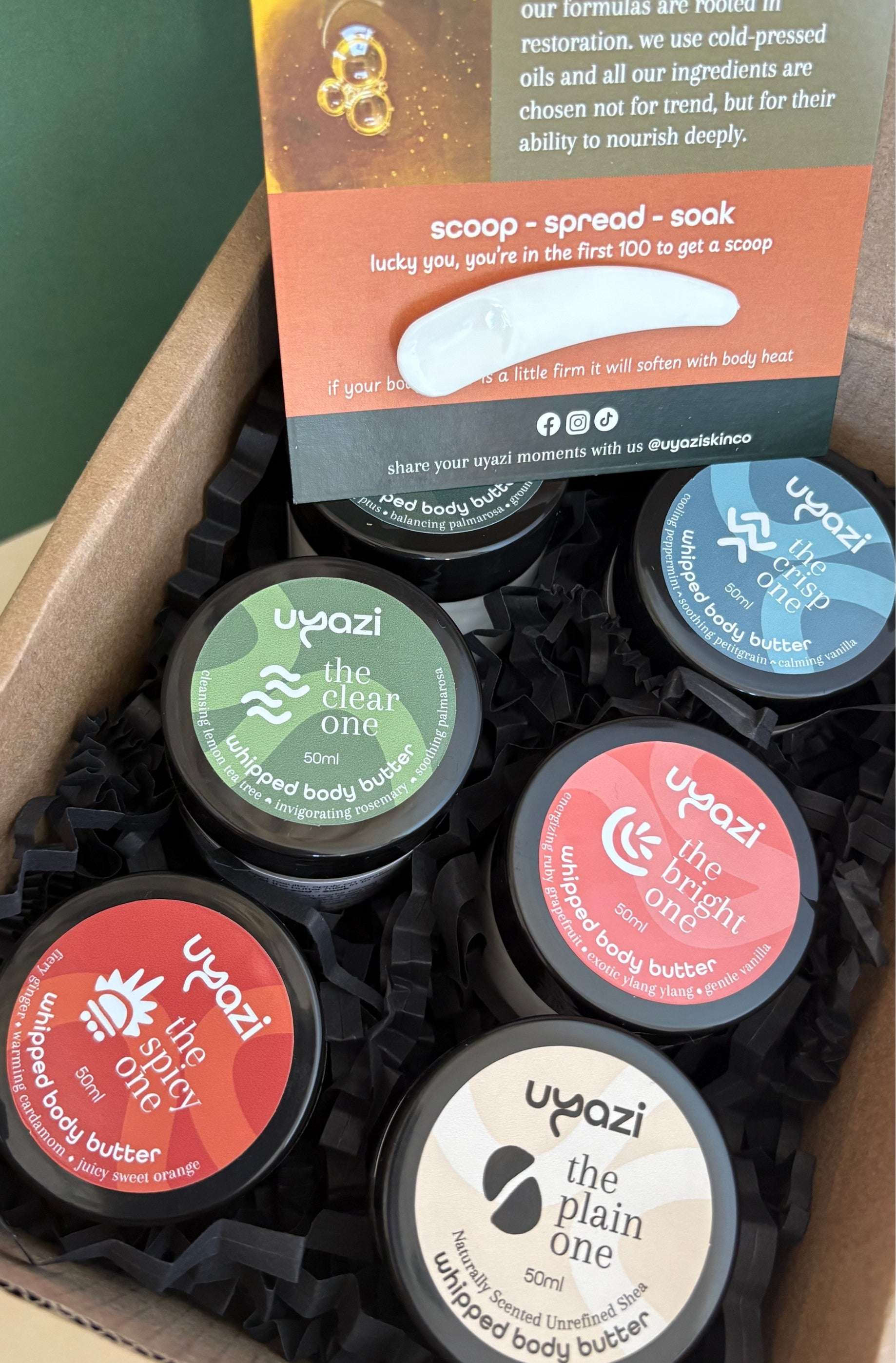 Collection of uyazi whipped body butter containers in a box with product packaging in the background.