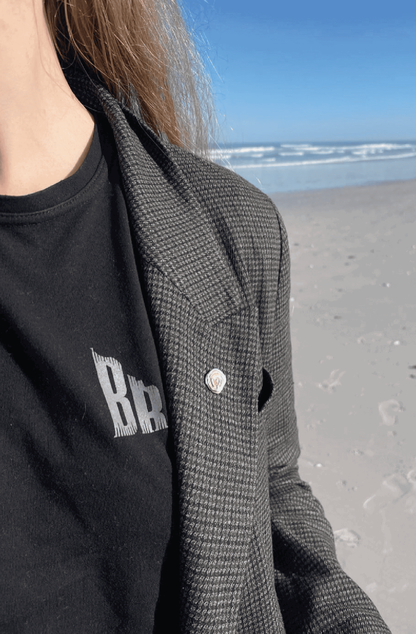 Woman on beach wearing a black t-shirt styled with tailored jacket and silver pin