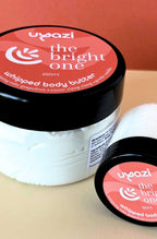 Uyazi whipped body butter jar with orange and peach label on a beige background