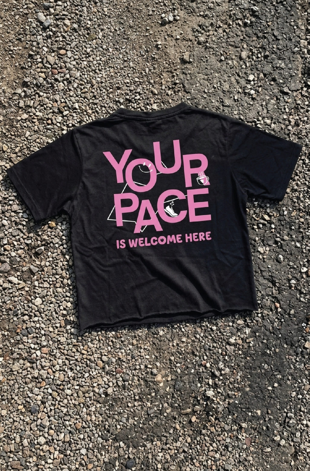 Black t-shirt with pink text 'YOUR PACE IS WELCOME HERE' on a textured surface