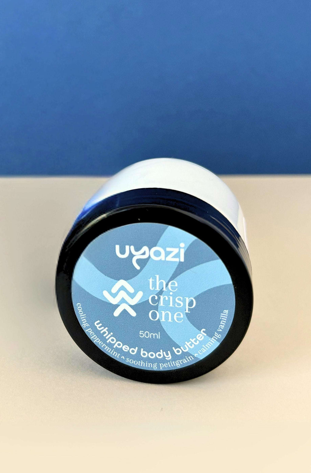 Uyazi whipped body butter jar on a beige surface with a blue background