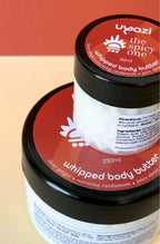 Two containers of Uzazi whipped body butter with red labels on a beige background
