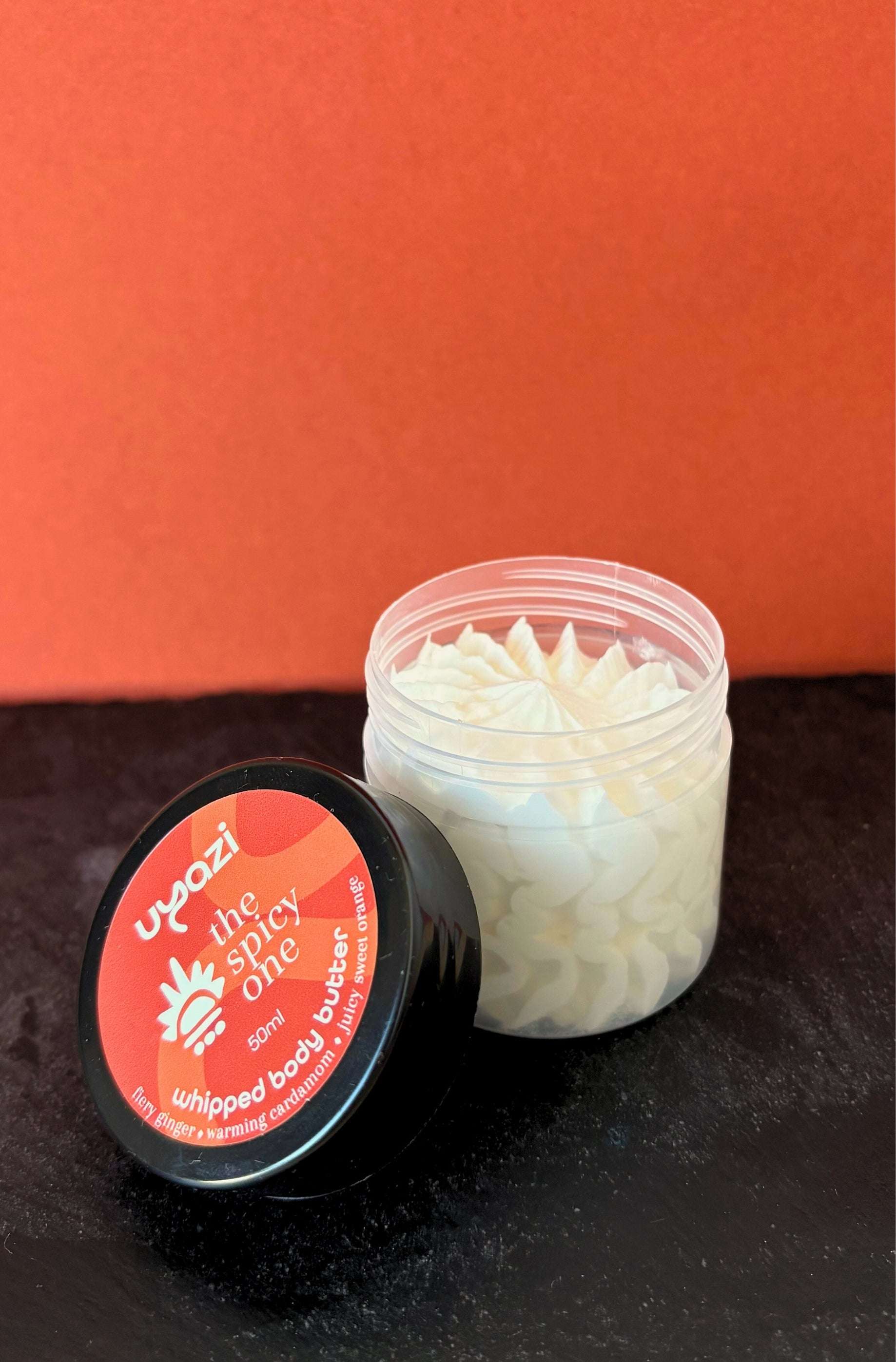 Jar of whipped body butter with a red label on an orange background