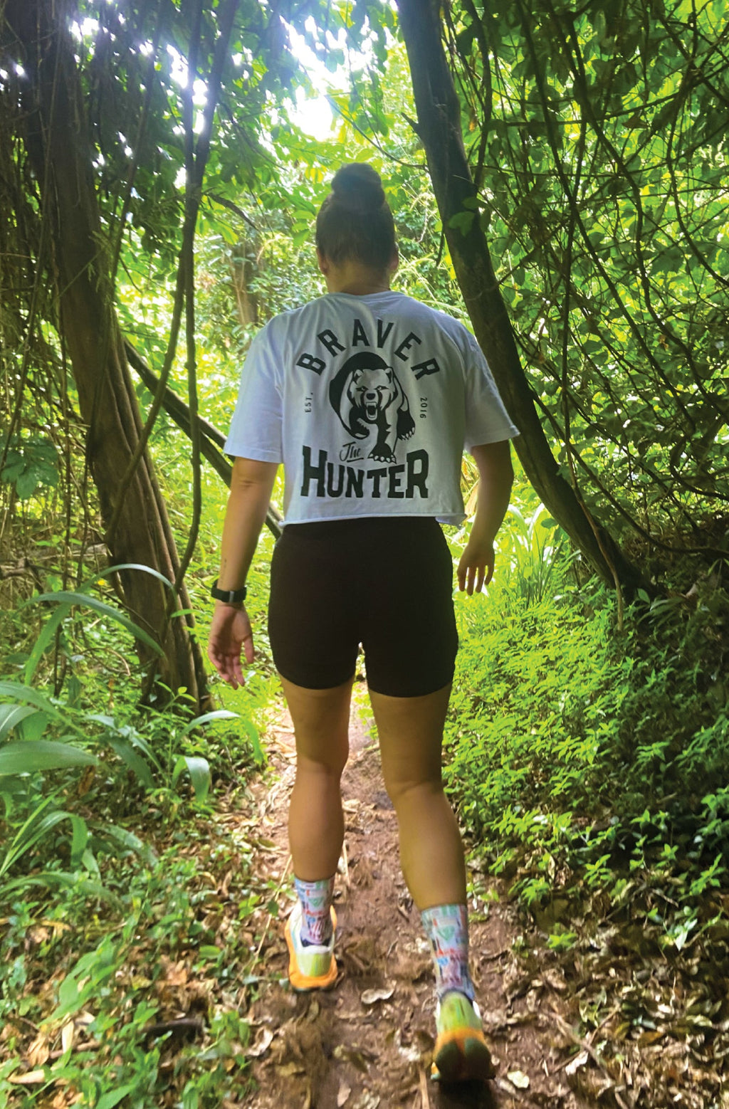 Person walking on a trail in a forest wearing a 'Braver Hunter' white graphic t-shirt.