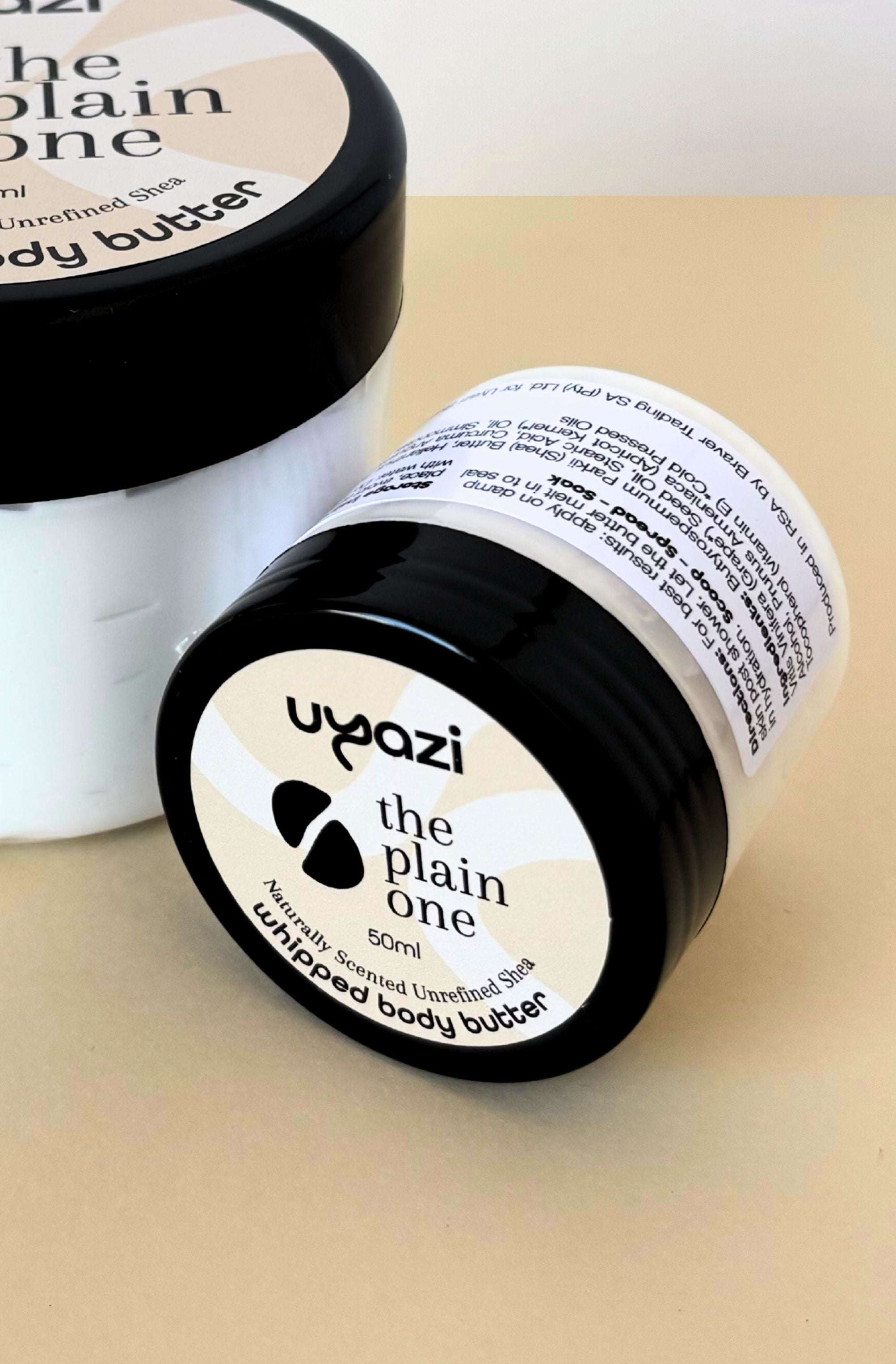 Two containers of uyazi 'the plain one' whipped body butter on a beige surface.