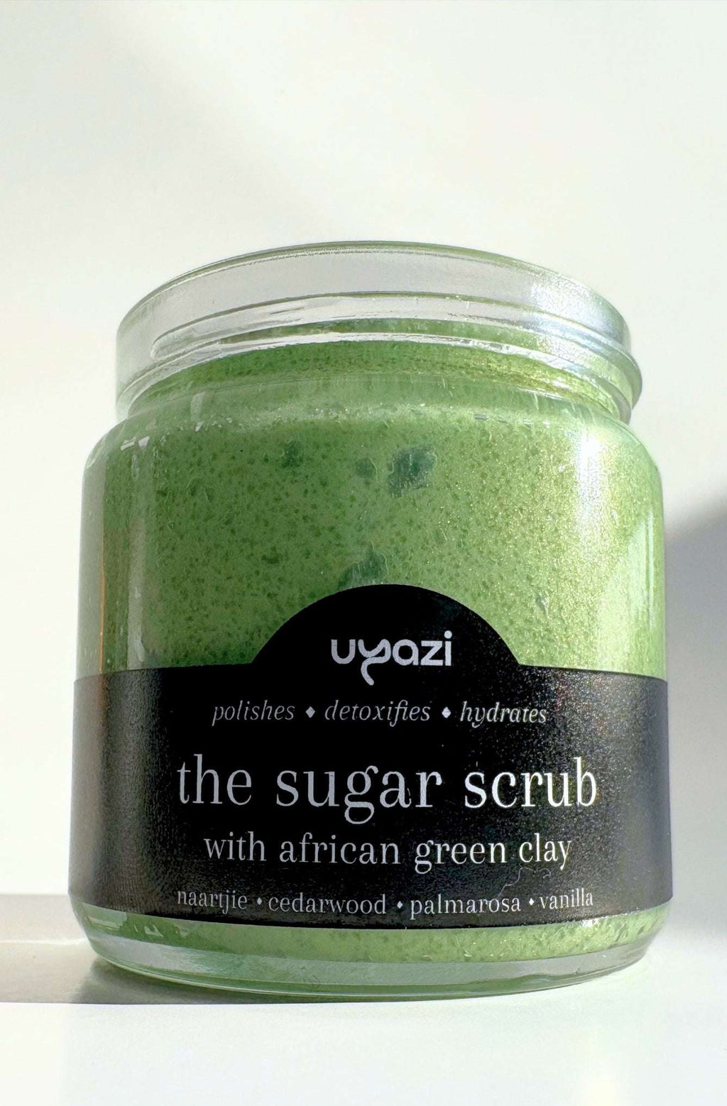 Jar of green sugar scrub with a black label on a white background