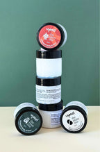 Stack of cosmetic jars filled with whipped body butter with visible branding on a green background