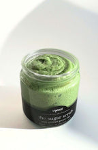 Jar of green sugar scrub with a black label on a white background