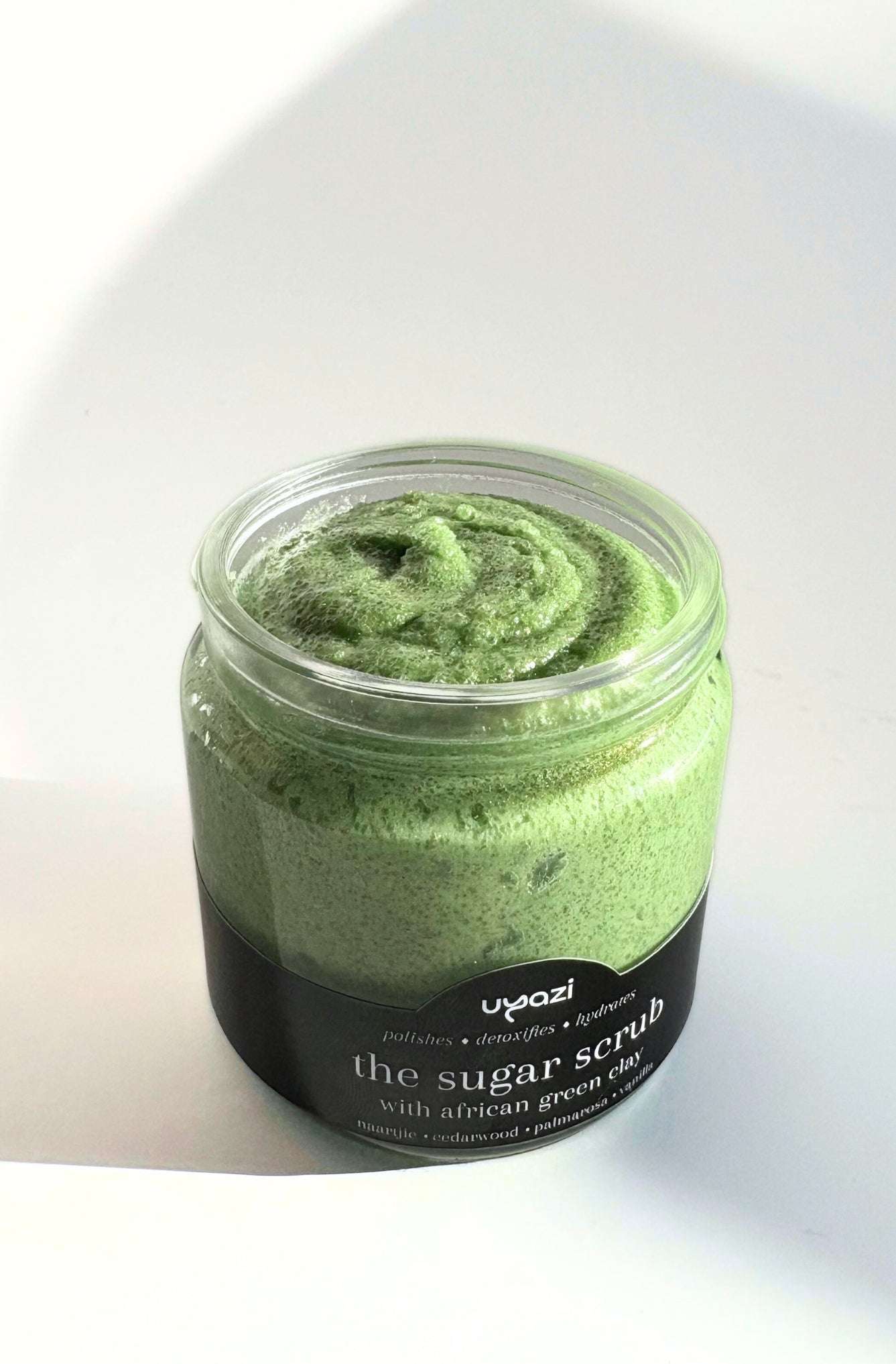Jar of green sugar scrub with a black label on a white background