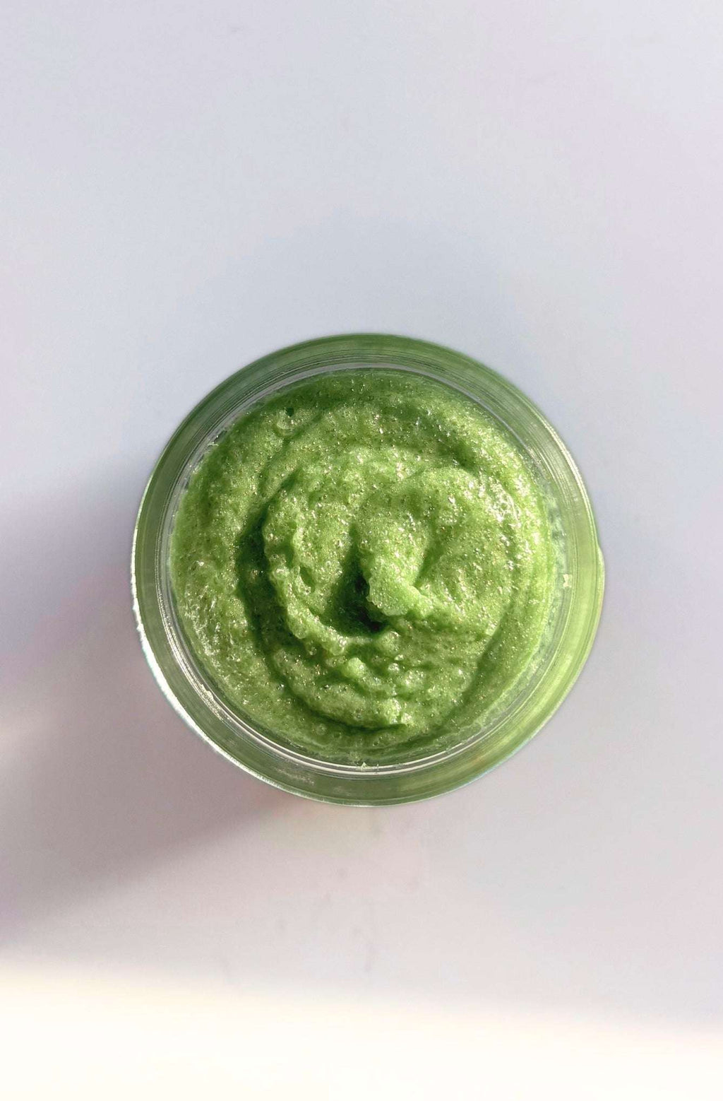 Green sugar scrub in a glass jar on white background